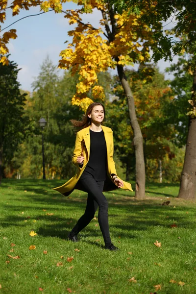Щаслива жінка в жовтому пальто, що йде осінньою вулицею — стокове фото