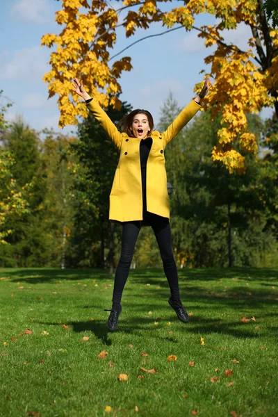Ευτυχισμένη γυναίκα σε κίτρινο παλτό άλμα στο πάρκο φθινόπωρο — Φωτογραφία Αρχείου