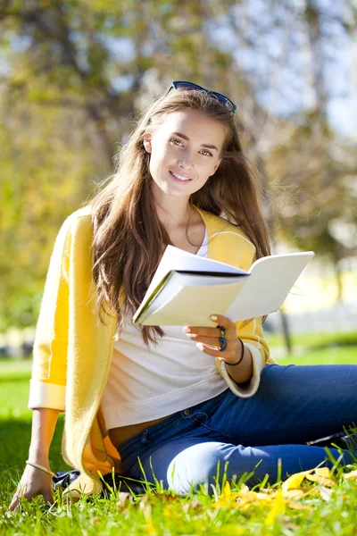 Hermosa estudiante sentada en el parque de otoño y leyendo un libro Imagen de stock