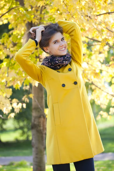 Happy young woman in yellow coat in autumn street — Stock Photo, Image