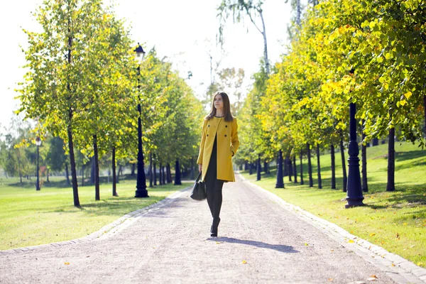 Счастливая женщина в желтом пальто ходит осенней улице — стоковое фото