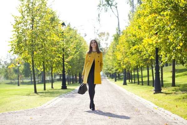 Щаслива жінка в жовтому пальто, що йде осінньою вулицею — стокове фото