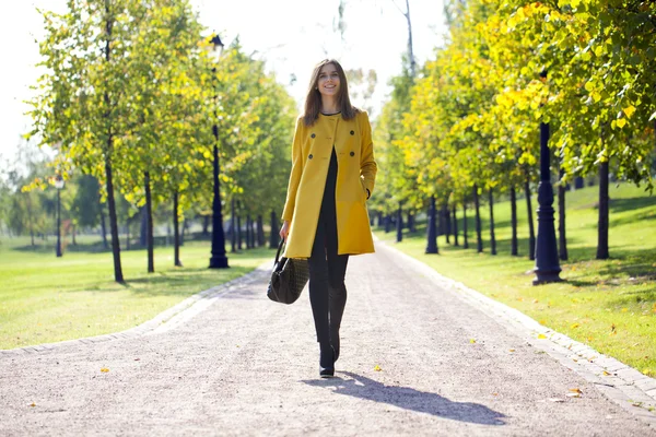 Happy woman in yellow coat walking autumn street — Stock Photo, Image