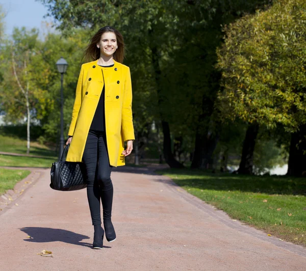 Happy young woman in yellow coat in autumn street — Stock Photo, Image