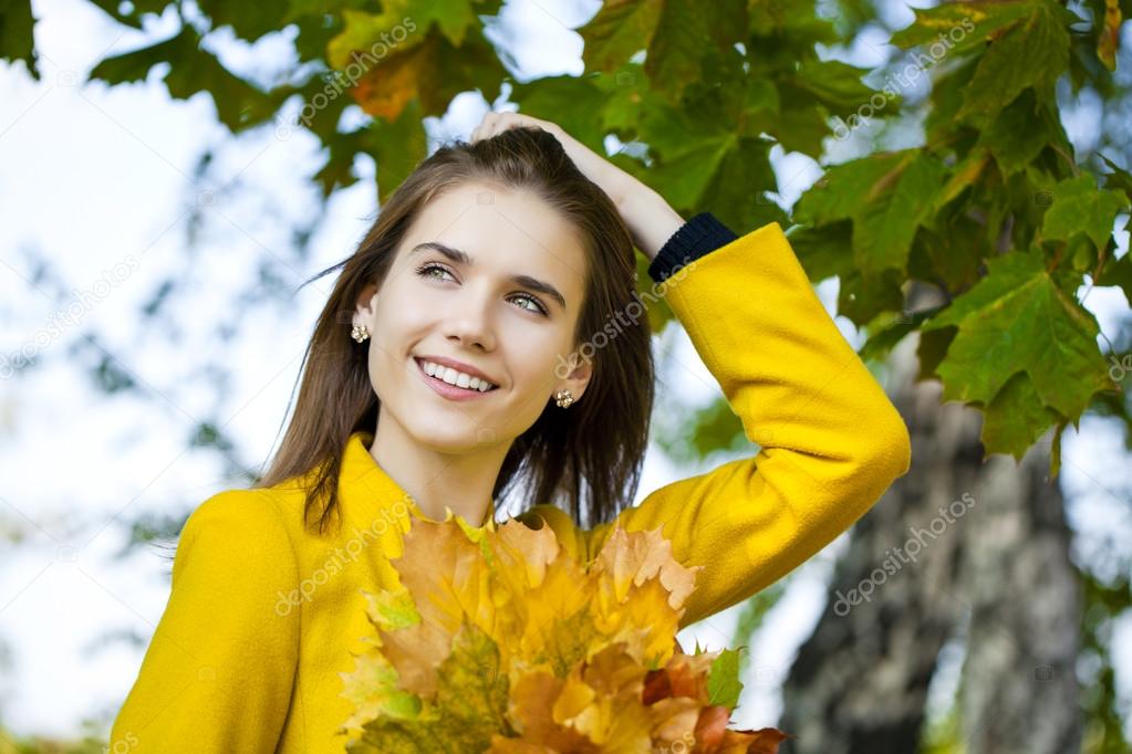 Happy young woman in yellow coat in autumn park