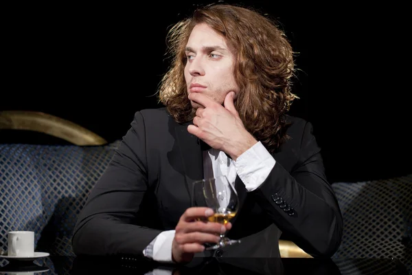 Elegantní mladý muž, který držel sklenici brandy koukal — Stock fotografie