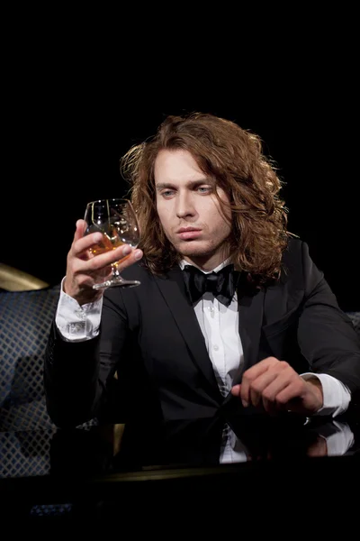 Elegancki, młody człowiek trzyma kieliszek brandy patrząc od — Zdjęcie stockowe