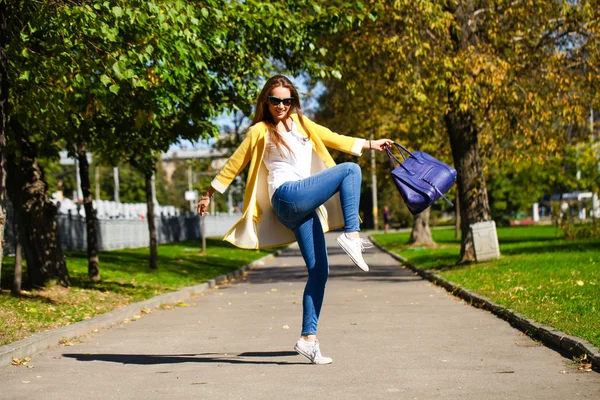 Glückliche Frau in gelbem Mantel spaziert durch die Herbststraße — Stockfoto