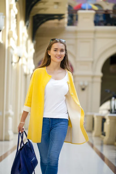 Νεαρή γυναίκα σε κίτρινο παλτό περπάτημα στο κατάστημα — Φωτογραφία Αρχείου