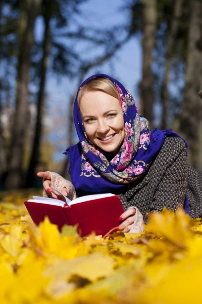 Bella ragazza sdraiata su foglie autunnali con libro rosso — Foto Stock