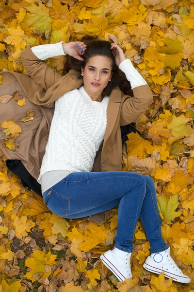 Молодая красивая девушка в синих джинсах лежит на желтых листьях — стоковое фото