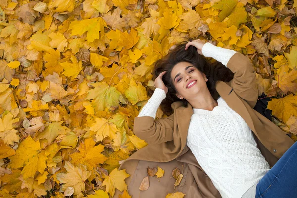 Young beautiful girl in blue jeans lying on yellow leaves — Stock Photo, Image