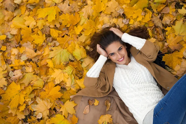 Young beautiful girl in blue jeans lying on yellow leaves — Stock Photo, Image