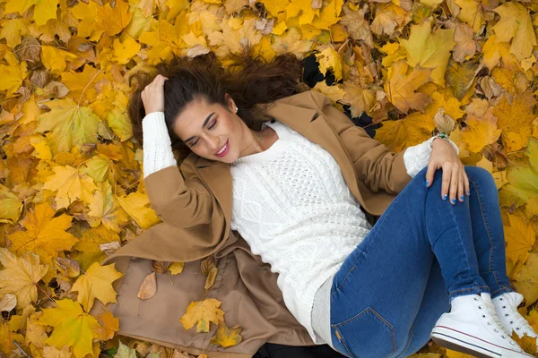 Молодая красивая девушка в синих джинсах лежит на желтых листьях — стоковое фото