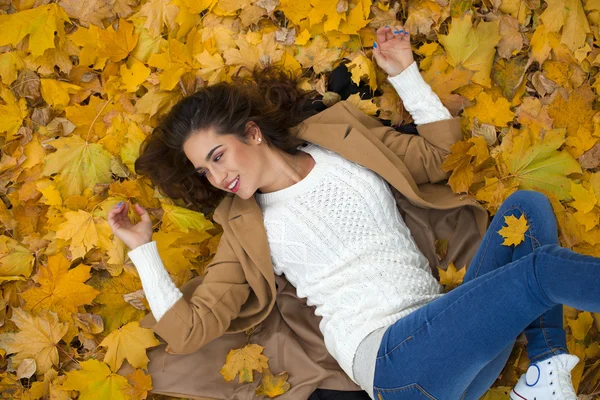 Junges schönes Mädchen in blauen Jeans auf gelben Blättern liegend — Stockfoto