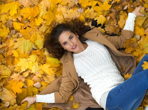 Young beautiful girl in blue jeans lying on yellow leaves — Stock Photo, Image