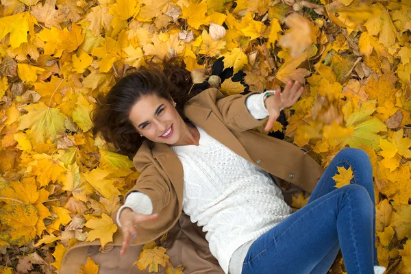 Mooi meisje in blue jeans liggend op gele bladeren — Stockfoto