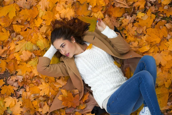 Young beautiful girl in blue jeans lying on yellow leaves — Stock Photo, Image