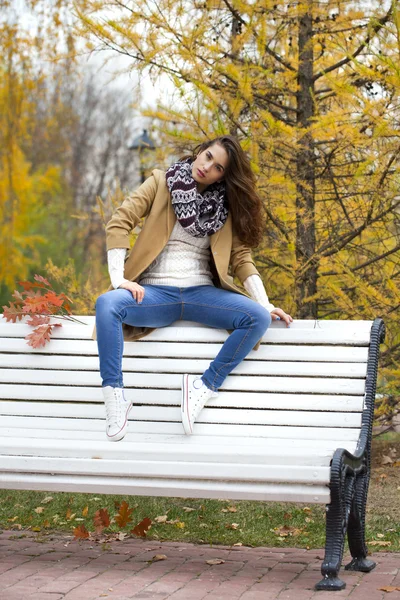 Mooie vrouw zittend op een bankje in de herfst park — Stockfoto
