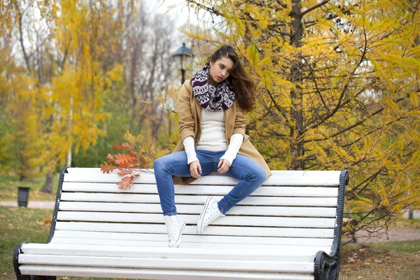 Krásná žena, sedící na lavičce v podzimním parku — Stock fotografie