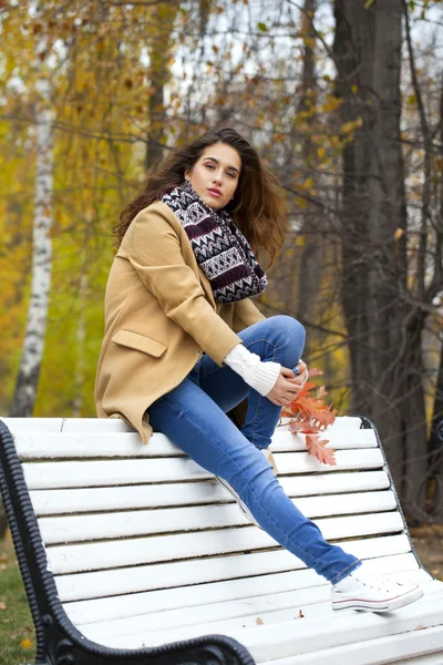 Mooie vrouw zittend op een bankje in de herfst park — Stockfoto