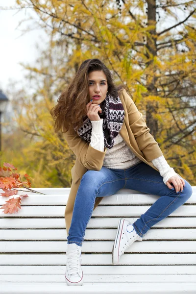 Hermosa mujer sentada en un banco en el parque de otoño — Foto de Stock