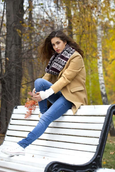 Schöne Frau sitzt auf einer Bank im Herbstpark — Stockfoto