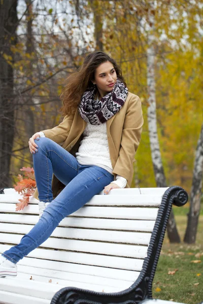 Hermosa mujer sentada en un banco en el parque de otoño — Foto de Stock