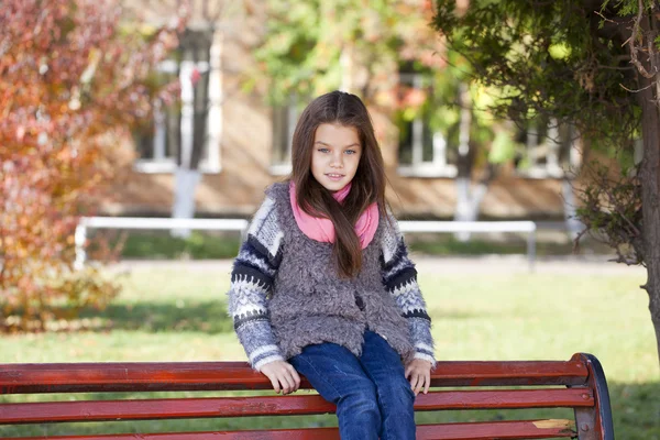 Güzel küçük bir kız bir bankta oturan — Stok fotoğraf
