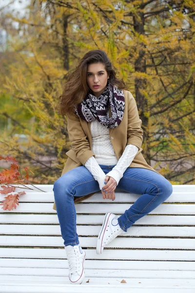 Hermosa mujer sentada en un banco en el parque de otoño — Foto de Stock