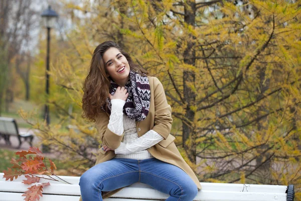 Mulher bonita sentada em um banco no parque de outono — Fotografia de Stock