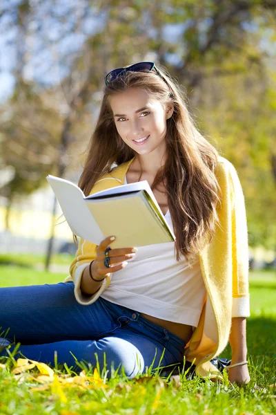Hermosa estudiante sentada en el parque de otoño y leyendo un libro — Foto de Stock