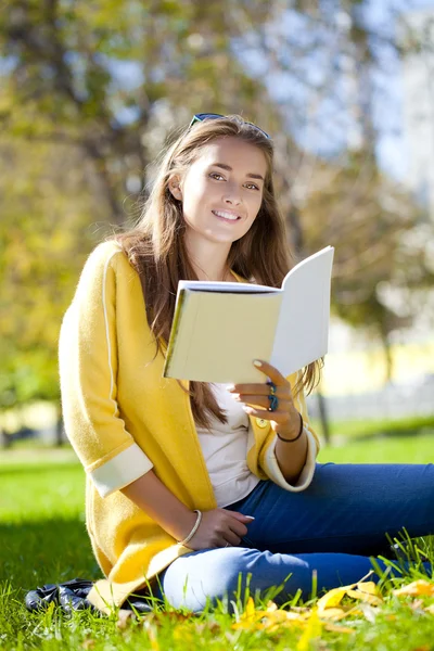 Beautiful schoolgirl sitting in autumn park and reading a book — Stock Photo, Image