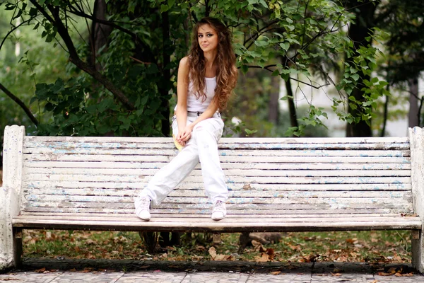 Mulher bonita sentada em um banco no parque de outono — Fotografia de Stock