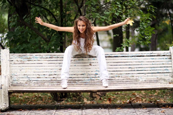 Mooie vrouw zittend op een bankje in de herfst park — Stockfoto