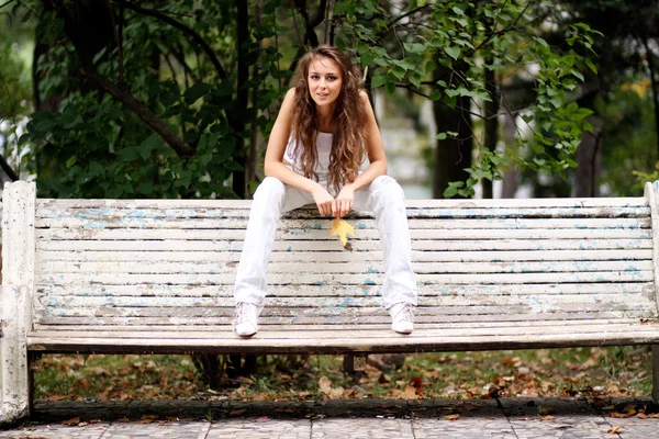 Vacker kvinna sitter på en bänk i höst park — Stockfoto