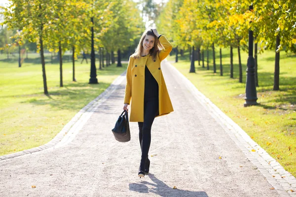 Femme heureuse en manteau jaune marchant rue d'automne — Photo