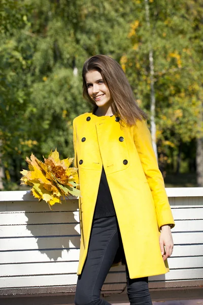 Happy young woman in yellow coat in autumn street — Stock Photo, Image