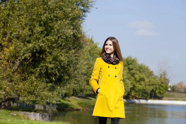 Happy young woman in yellow coat in autumn street — Stock Photo, Image