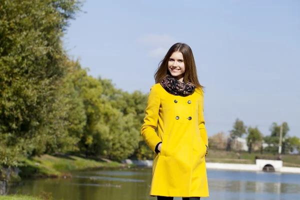 Happy young woman in yellow coat in autumn street — Stock Photo, Image