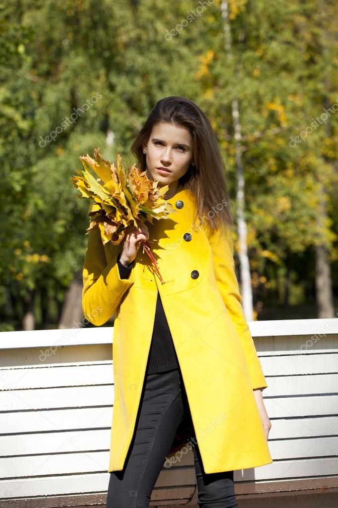 Happy young woman in yellow coat in autumn street