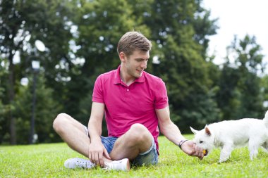 Genç adam parkta köpeğiyle oynuyor.