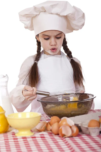 Little girl in a white apron breaks near the plate with eggs — Stock Photo, Image