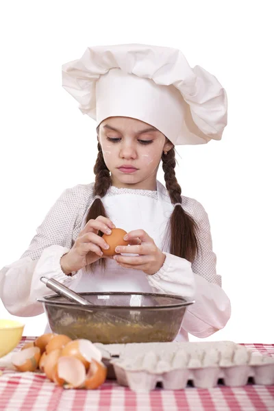 Malý kuchař dívka v bílé zástěře rozbije vejce v deep dish — Stock fotografie