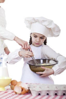 Küçük kız cook fırçalamak yumurta büyük bir tabak içinde kamçı.