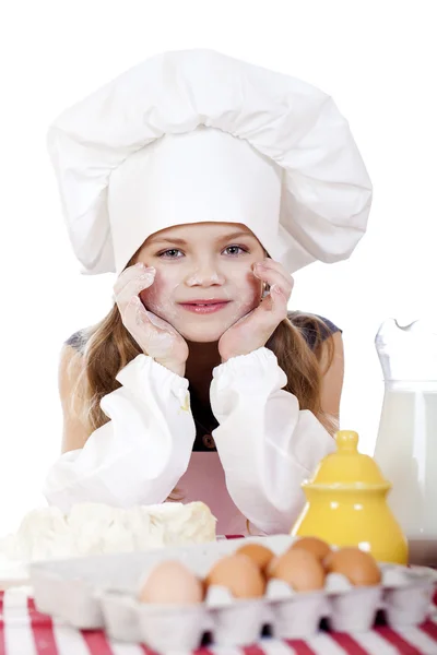 Маленькая девочка в белом фартуке ломается возле тарелки с яйцами — стоковое фото