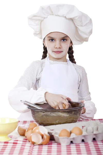 Little cook girl in a white apron breaks eggs in a deep dish — Stock Photo, Image