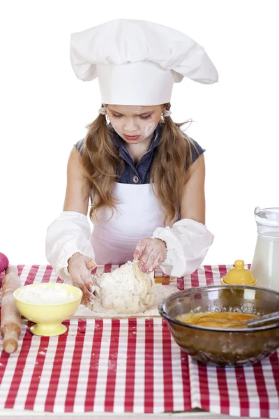 Liten flicka i en vit förkläde och kockar hatt knåda degen i th — Stockfoto