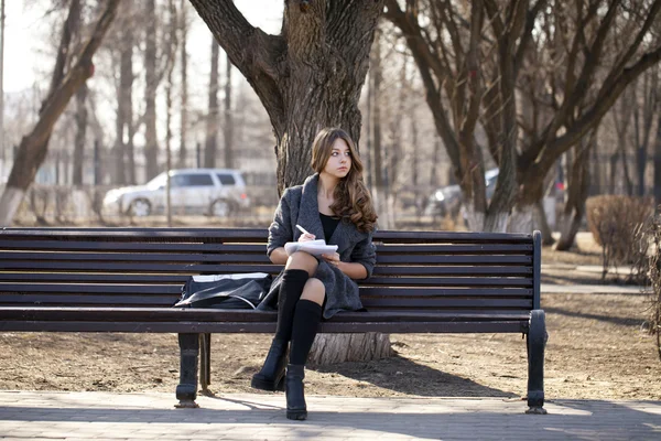 春パークでノートのベンチに座っている女子高生 — ストック写真