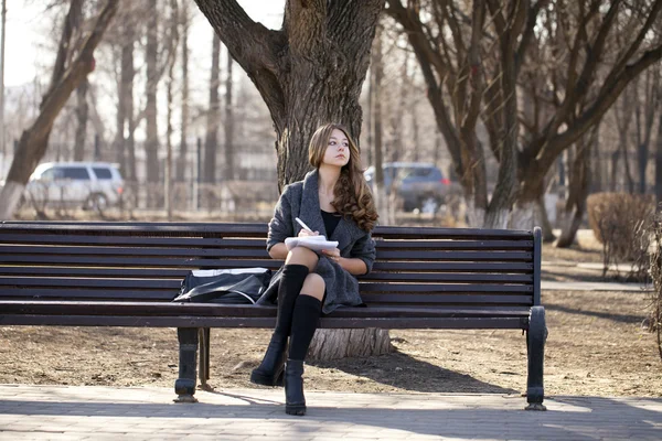 Estudante sentado em um banco com um caderno no parque da primavera — Fotografia de Stock